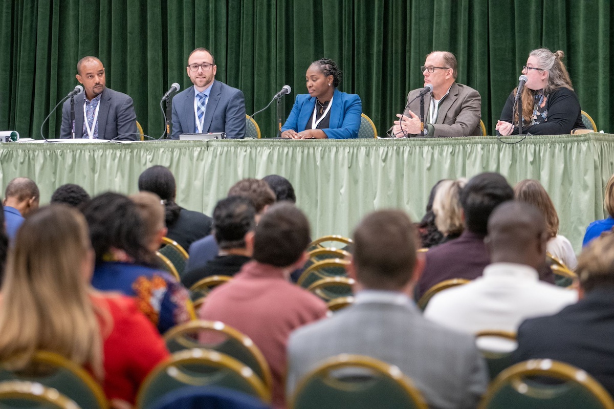 Five people sitting on a stage speaking to an audience. 