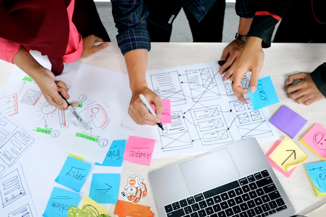 Decorative image: aerial view of people working on project with diagrams, sticky-notes, and a laptop