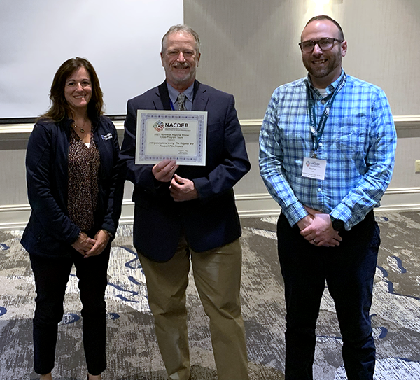 Three people standing, with middle person holding certificate