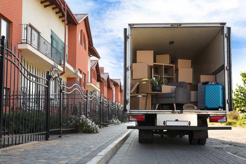 Moving van full of boxes, parked outside a row of townhomes. 
